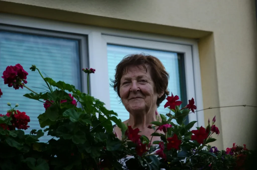 Signora anziana alla finestra fra i gerani, mamma che riceve fiori a casa